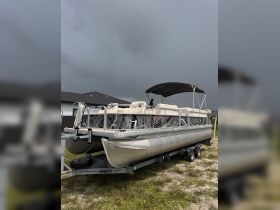 A sleek pontoon boat is parked on its trailer, showcasing its spacious seating and stylish design, perfect for leisurely days on the water.