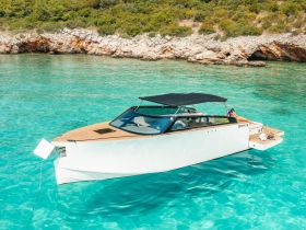 A stylish boat glides through crystal-clear turquoise waters, with a guest lounging on the deck, perfect for a relaxing day on the water.