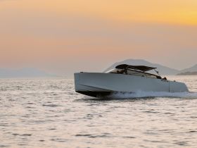 A sleek speedboat glides through calm waters at sunset, showcasing its modern design against a picturesque backdrop of mountains.
