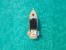 An aerial view of a stylish boat with a sunbather relaxing on the deck, surrounded by crystal-clear turquoise waters — a perfect scene for a luxurious day on the water.