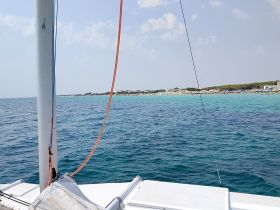 A picturesque view from a catamaran showcasing a beautiful coastline and beach, perfect for a relaxing day on the water.