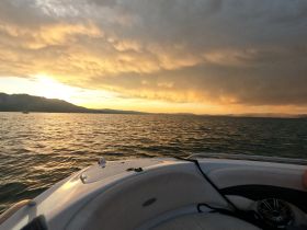A serene sunset view from the bow of a boat, showcasing tranquil waters and distant mountains — perfect for peaceful evening cruises.