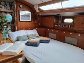 Cozy interior of a boat cabin featuring a comfortable bed, decorative pillows, and a reading area, perfect for relaxing during a sailing trip.