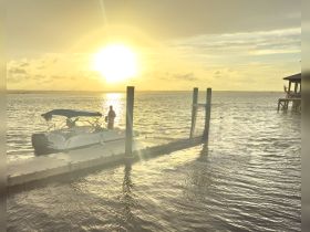 A serene sunset view featuring a boat docked as a person enjoys fishing, creating a picturesque moment on the water.