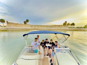 A cheerful group enjoys a boat ride with a scenic backdrop of historic fortifications, perfect for family outings and celebrations on the water.