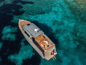 An aerial view of a stylish boat anchored in stunning turquoise waters, with guests relaxing on the deck — a perfect setting for a luxurious day on the water.