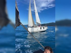 A sailboat glides through vibrant blue waters, with guests enjoying the experience on board — perfect for sailing adventures and family outings.