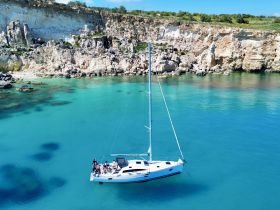 A group enjoys a sailing adventure on a beautiful turquoise bay, surrounded by stunning cliffs — perfect for exploring the coastline and enjoying the sun.