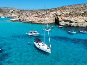 A vibrant scene of boats anchored in crystal-clear waters near a picturesque beach, showcasing a lively day of swimming and sailing in a stunning coastal destination.
