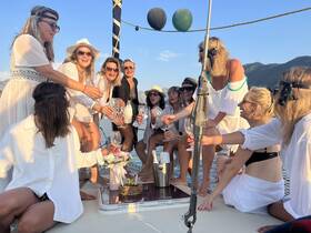 A lively group of women celebrates a 40th birthday aboard a yacht, toasting with cocktails and enjoying the beautiful scenery.
