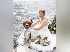 A beautiful bride poses with her beagle on a boat, showcasing a unique wedding moment surrounded by floral arrangements — perfect for memorable celebrations on the water.