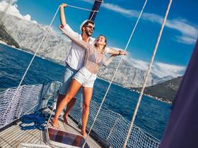A joyful couple enjoys a sailing adventure, embracing the moment on the deck of a boat with stunning mountain views in the background.