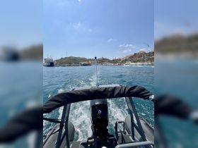 A view from the back of a speedboat cruising through clear waters, showcasing the vibrant marina and hills in the background — perfect for exploring coastal destinations.