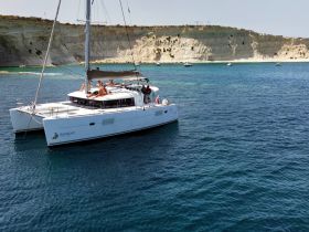 A lively group enjoys sunbathing on a catamaran near a stunning coastline, perfect for summer adventures and relaxation on the water.