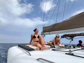 Two friends relax and sunbathe on the deck of a catamaran, enjoying a beautiful day at sea — perfect for a fun day out with friends.