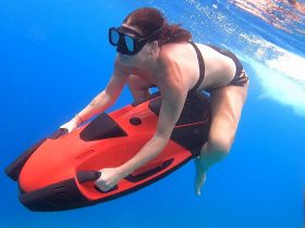 A woman enjoys an exhilarating underwater ride on a jet ski, showcasing the thrill of snorkeling adventures in crystal-clear waters.