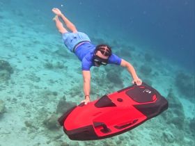 An adventurous diver explores the underwater world while using a water scooter, showcasing the thrill of snorkeling and diving in crystal-clear waters.