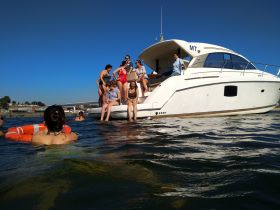 A lively group enjoys a sunny day on the water, with some swimming and others relaxing on the boat — perfect for summer fun and memorable outings.