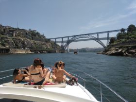 A lively group enjoys a sunny day on a boat, taking in the scenic views of a stunning bridge and rocky coastline — perfect for summer outings and adventures on the water.