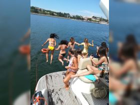 A lively group of friends jumps off the side of a boat into the water, capturing the excitement of a fun-filled day on the water.