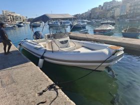 A center console boat named 'CLUBMAN 24' docked at a marina, showcasing its sleek design and surrounding boats in the background.