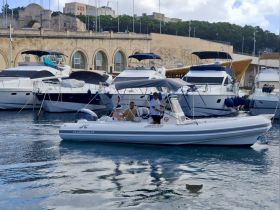 A small boat navigates through a harbor filled with yachts, showcasing a lively atmosphere with people onboard, perfect for exploring coastal destinations.