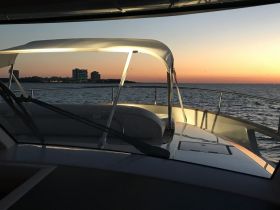 A serene view from the helm of a boat at sunset, showcasing the sleek interior and the tranquil waters ahead, perfect for evening cruises.