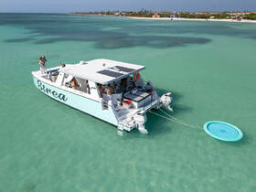 A lively group enjoys a day on the water aboard the Strea, with a floating mat nearby, perfect for fun and relaxation in the turquoise waters.