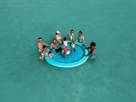 A joyful family enjoys a fun day in the water on a floating mat, surrounded by the stunning turquoise sea — perfect for creating unforgettable summer memories.