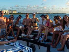 A lively group of friends enjoys a sunset cruise on a boat, celebrating with drinks and good company — perfect for unforgettable summer memories.