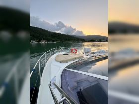 A serene view from the front of a yacht, showcasing the vessel's sleek design against a backdrop of lush greenery and a tranquil harbor at sunset.