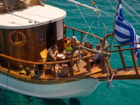 A group enjoys a meal on the deck of a boat, surrounded by stunning turquoise waters — a perfect setting for relaxation and socializing on the sea.