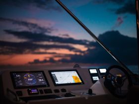 A close-up view of a boat's helm and console, showcasing navigational displays against a stunning sunset backdrop — perfect for those who love boating technology.