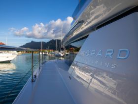A sleek Leopard catamaran docked in a marina, showcasing its elegant design against a backdrop of mountains and clear blue skies.