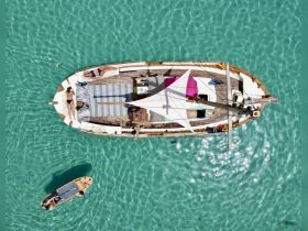 Aerial view of guests sunbathing on a boat in crystal-clear turquoise waters, showcasing a perfect day of relaxation and fun on the water.