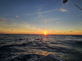 A stunning sunset over the ocean, captured from the deck of a boat, showcasing the tranquil beauty of a maritime evening.