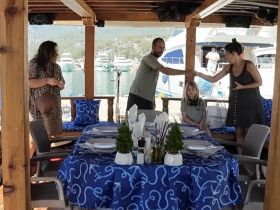 A group gathers at a beautifully set dining area on a boat, engaging in a warm handshake and conversation, perfect for celebrations and gatherings on the water.