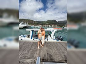 A couple poses happily at a marina beside their boat, capturing a memorable moment during their vacation amidst stunning coastal scenery.