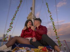A romantic moment between a couple on a sailboat, enjoying a picnic with a beautiful sunset backdrop — perfect for special occasions or intimate sailing experiences.