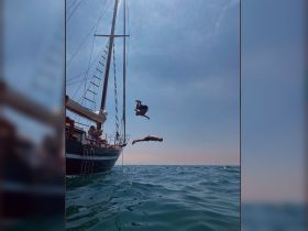 Two individuals leap off a sailboat into the sparkling sea, capturing the thrill of summer adventures on the water.