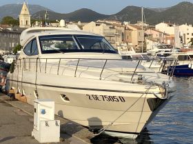 A sleek yacht docked at the marina, showcasing its elegant design against a scenic backdrop of coastal buildings and mountains.