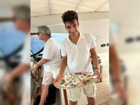 A young crew member presents a beautifully arranged platter of gourmet appetizers aboard a yacht, showcasing the luxurious catering options available for guests.