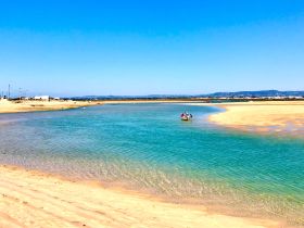 A picturesque scene of a small boat with people enjoying a sandbar stop in clear turquoise waters, surrounded by sandy shores and a beautiful landscape.