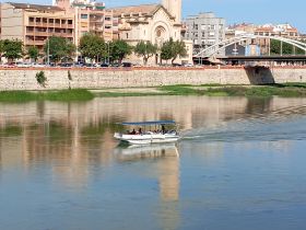 A small boat navigates the river, showcasing a vibrant cityscape in the background — perfect for scenic tours and leisurely outings.
