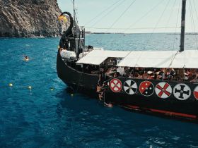 A lively scene aboard a unique boat with guests enjoying the sun and water activities, including swimming and kayaking, perfect for a fun day on the ocean.