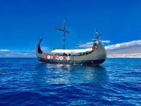 A striking Viking ship sails through clear blue waters, showcasing its unique design and historical charm — perfect for themed tours or maritime adventures.