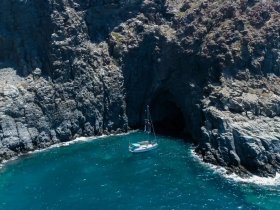 A stunning aerial view of a sailboat anchored near a rocky coastline, showcasing the beautiful turquoise waters and dramatic cliffs — perfect for exploring hidden coves.