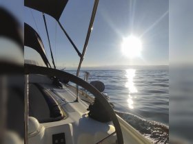 A serene view from the helm of a sailboat, capturing the bright sun reflecting on calm waters — perfect for a peaceful day at sea.