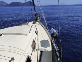A clear view of a sailboat's deck as it glides through calm blue waters, showcasing the vessel's sleek design and the serene maritime environment.