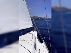 A scenic view from the bow of a sailboat, showcasing the vessel in motion against a backdrop of clear blue waters and distant hills.
